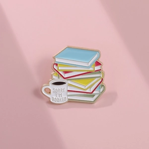 Detail of enamel pin featuring colorful books and a coffee cup with Sorry I'm Booked text