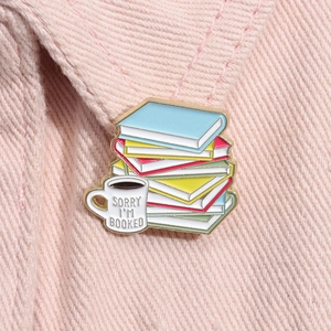 Dettaglio macro della spilla in smalto con libri e tazza di caffè su tessuto rosa