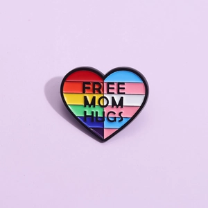 Dettaglio della spilla a cuore Free Mom Hugs con colori della bandiera LGBTQ+ su sfondo viola