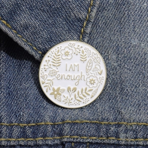 Close-up of 'I AM enough' enamel pin with gold floral art on blue denim jacket