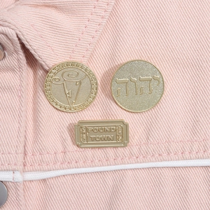 Detailed macro view of vintage metal pins with cloud motifs and Hebrew text on denim