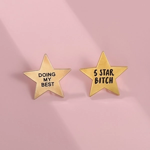 Detailed macro view of two golden pentagram enamel pins with humorous engraved text