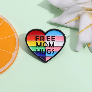 Dettaglio della spilla in smalto a cuore arcobaleno Free Mom Hugs su sfondo verde