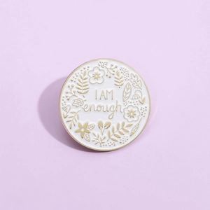 White enamel pin with 'I AM enough' quote and golden floral details on purple background