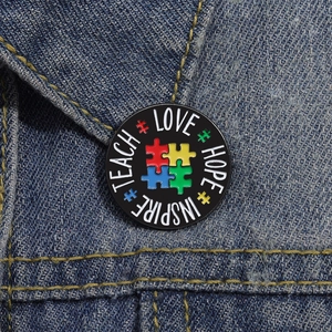 Rainbow puzzle piece enamel brooch with teach love hope inspire words on denim