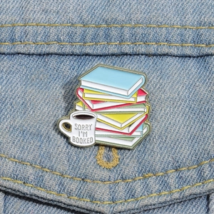 Enamel book stack brooch with coffee cup and Sorry I'm Booked text on denim backdrop