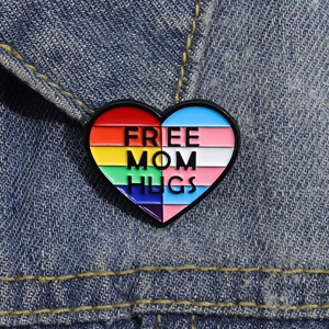 Macro della spilla a cuore in smalto 'FREE MOM HUGS' su una giacca di jeans blu