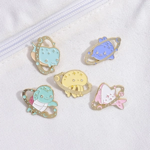 Detailed close-up of 5 pastel enamel pins with ocean and galaxy motifs on white fabric