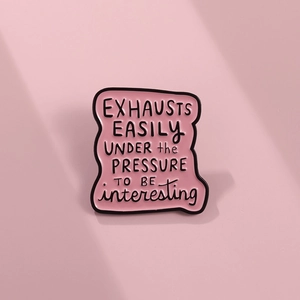Macro detail of pink enamel pin badge with humorous quote Exhausts Easily under pressure