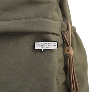 Detail of speech bubble enamel pin on olive green fabric showing haunted message text