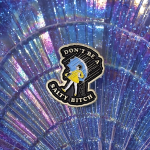 Detail of enamel pin featuring a girl in yellow raincoat with 'Don't be a salty bitch' text