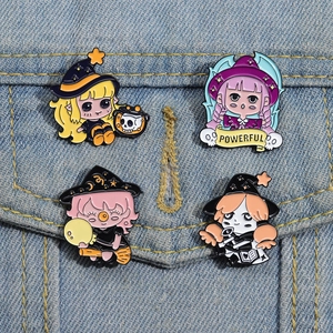 Set of four cartoon magic girl enamel pins with witch hats on denim fabric background