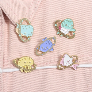 Detail of five cute cartoon ocean animal enamel pins with space rings on pink denim fabric
