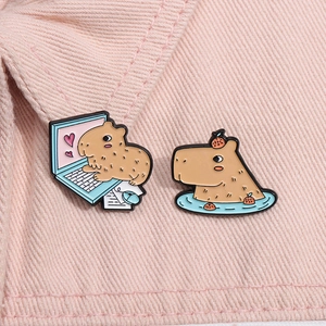 Close-up of cute enamel capybara pins with laptop and spa theme on pink fabric