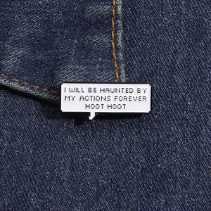 Detail of the rectangular enamel pin featuring pixel art text on a denim jacket