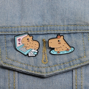 Detail of cute capybara enamel pins featuring laptop and bath scenes on denim fabric