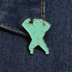 Detail of funny muscular frog enamel pin on dark blue denim fabric pocket edge