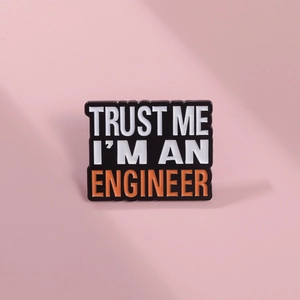 Detail of Trust Me I'm An Engineer enamel brooch with white and orange text on black
