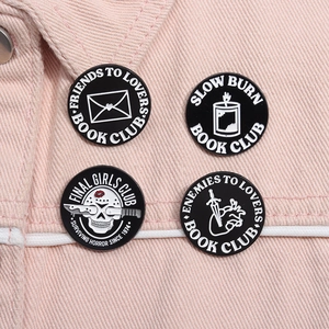 Detailed view of four literary and horror enamel pins on pink denim fabric background