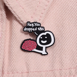 Dettaglio della spilla in smalto con testo 'Hey, You dropped this' su denim rosa