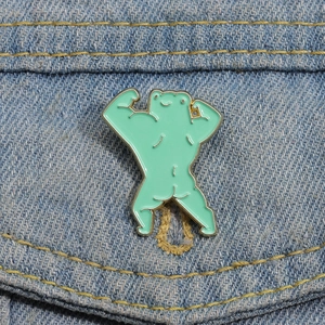 Creative mint green muscular cartoon frog enamel pin displayed on blue denim fabric