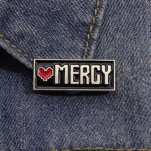 Dettaglio della spilla smaltata MERCY con cuore pixelato su tessuto denim