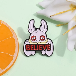 Mini purple moth enamel pin with red eyes and Believe lettering on a green background