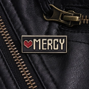 Dettaglio della spilla Mercy pixel art smaltata con cuore rosso su pelle nera