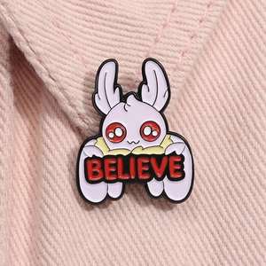 Detail of pink moth enamel pin with BELIEVE sign pinned on denim fabric jacket