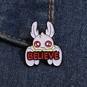 Detailed view of Mothman enamel pin with Believe sign on dark denim jacket fabric
