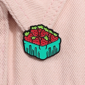 Détail d'une épingle émaillée panier de fraises sur un tissu en velours côtelé rose