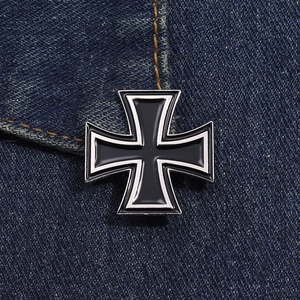 Close-up of industrial retro iron cross metal badge pin on blue denim fabric background