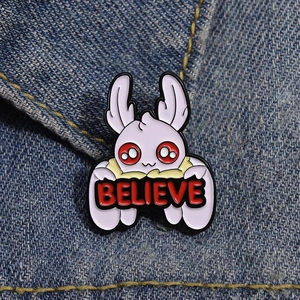Creative white creature enamel pin with red eyes and Believe banner on denim fabric