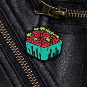 Détail d'une broche en émail représentant un panier de fraises sur une veste en cuir noir