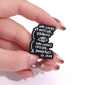 Detailed view of black enamel pin with C.G. Jung quote and eye graphic on white background