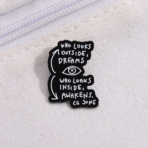 Detailed macro view of black enamel pin with C.G. Jung quote on white canvas fabric