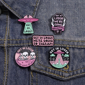 Detail of five funny enamel pins with Get in Loser slogan on blue denim fabric background