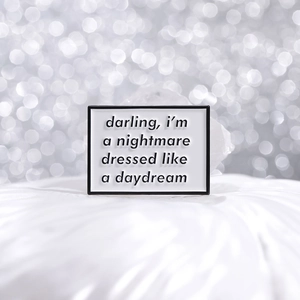 Macro detail of enamel brooch with nightmare dressed like a daydream text on white fabric