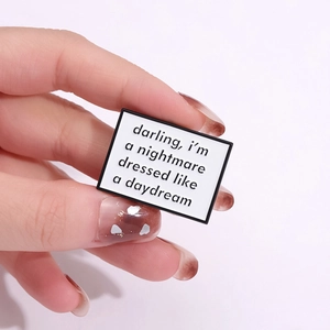 Macro shot of rectangular enamel pin with text darling i am a nightmare dressed like a daydream