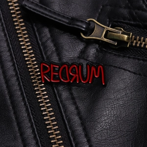 Macro view of REDRUM enamel pin with red dripping text on a black leather jacket