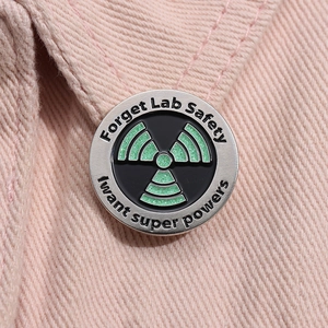 Macro shot of Forget Lab Safety science enamel pin on pink denim fabric with green glitter