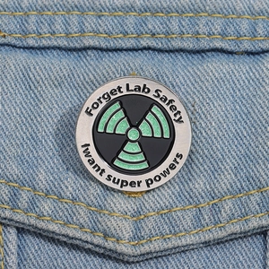 Macro detail of Forget Lab Safety science enamel pin with glitter radioactive sign on denim