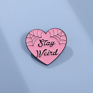 Pink heart enamel pin with Stay Weird text and black spider web patterns for punk style