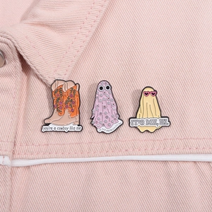 Close-up of pastel enamel pins with floral cowboy boots and ghost designs on pink denim jacket