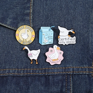 Détail de cinq pin's en émail Silly Goose présentés sur un tissu en denim bleu foncé