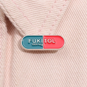 Macro shot of a blue and red enamel pill brooch featuring FUKITOL text on pink denim jacket