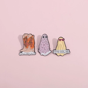 Detailed macro view of three enamel pins featuring floral cowboy boots and ghost designs
