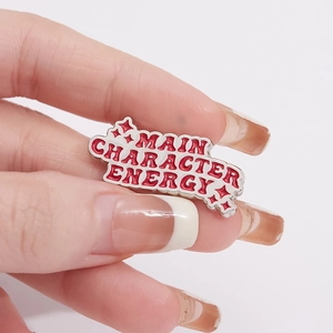 Emaille speld met rode Main Character Energy tekst en sprankelende sterren op wit