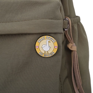 Détail de l'épinglette émaillée Silly Goose sur fond jaune posée sur un sac en tissu