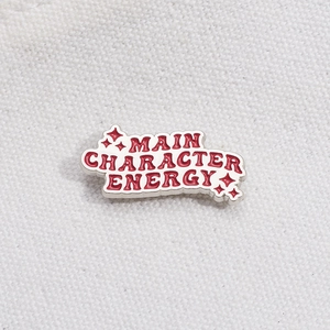 Emaille speld met Main Character Energy tekst en sterdetails op canvas achtergrond